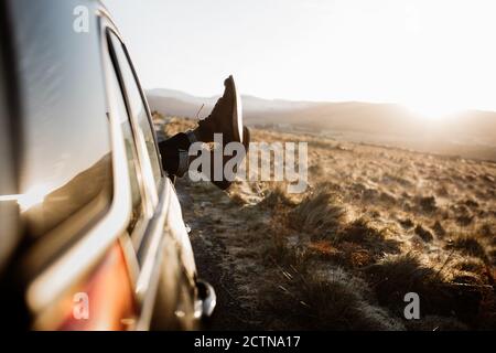 unrecognizable tourist lying in car with legs out of window on background of sunrise in Scottish Highlands Stock Photo