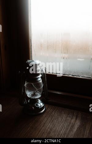 Cozy atmosphere of room with retro oil lantern placed on windowsill with misted window in house Stock Photo