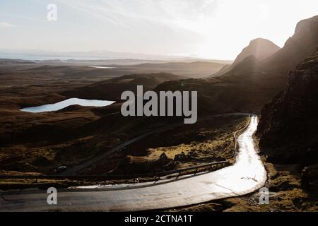 Spectacular landscape of mountains and winding road under cloudy sky with bright sun in morning in Scottish Highlands Stock Photo