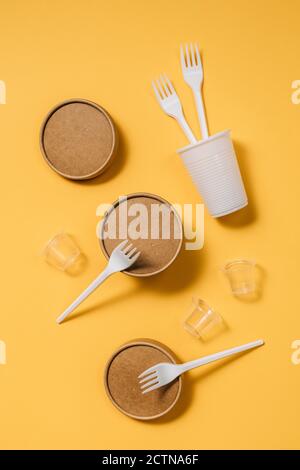 High angle of cardboard containers with plastic forks and spoons arranged with small plastic cups for takeaway food service on orange table Stock Photo