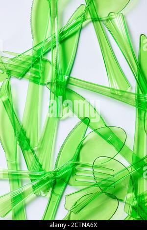 Top view composition of bright green transparent plastic forks and spoons and knives placed on white background Stock Photo