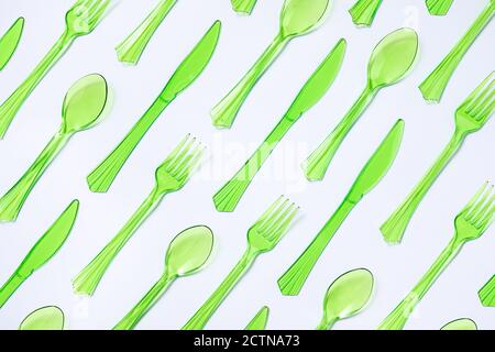 Top view composition of bright green transparent plastic cups with forks and spoons and knives placed on white background Stock Photo
