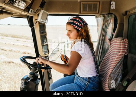 Side view of serious female farmer operating combine harvester and collecting wheat in field in rural area Stock Photo