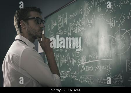 Mathematician reviewing math formulas on the chalkboard, he is thinking with hand on chin Stock Photo