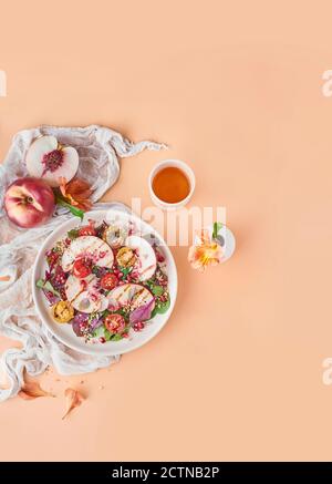 Top view of tasty salad with peaches and cherry tomatoes garnished with greenery and served on pink background in studio Stock Photo