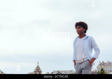 Stylish black male with Afro hairstyle walking with hands in pockets on street and smiling e looking away Stock Photo