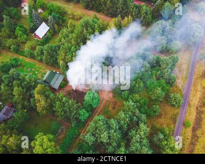 Smoke from the fire over cottages in the forest. Drone, aerial View. Stock Photo