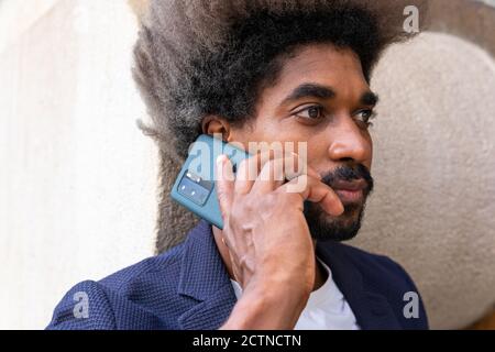 Side view portrait of an african man in suit using his mobile phone in front of a wooden wall Stock Photo