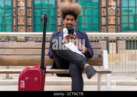 African man in suit using his mobile phone sitting in a wooden bench Stock Photo