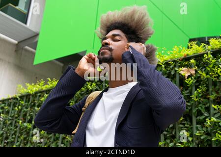 Black man with afro hair closing his eyes his while listening to music with a wireless headset on the street Stock Photo