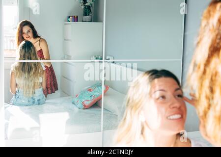 Smiling Woman doing makeup for content female friend sitting on bed at home Stock Photo