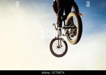 Urban biker performing acrobatic jump at sunny sky - Guy riding bmx bicycle at extreme sport competition on sunny afternoon - Alternative lifestyle concept on warm sunshine colors. Stock Photo