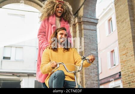 Happy couple riding on bicycle in the city center - Young people having fun sharing time together outdoor Stock Photo