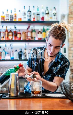 Focused male bartender with dreadlocks pouring alcohol in glass and preparing delicious cocktail at counter in bar Stock Photo