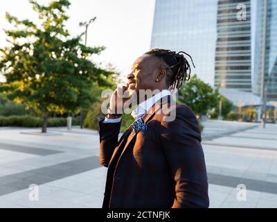 Black businessman standing in downtown and speaking on mobile phone while discussing work issues and looking away Stock Photo