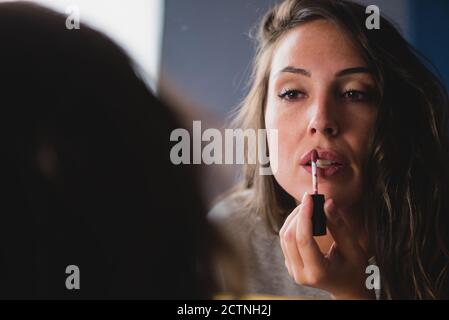 Concentrated charming female with smooth skin applying gloss lipstick while preparing for event Stock Photo