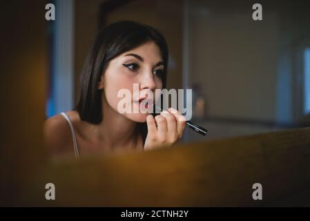 Concentrated charming female with smooth skin applying red lipstick while preparing for event Stock Photo