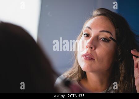 Concentrated charming female with smooth skin applying mascara while preparing for event Stock Photo