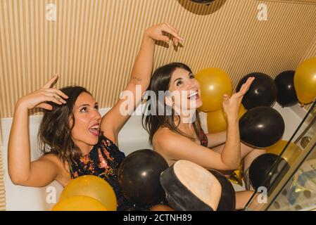 From above of young female in festive dress sleeping in bathtub filled with colorful balloons after holiday celebration Stock Photo