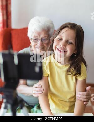 Smiling senior Woman and girl sitting in living room together and having video call on smartphone Stock Photo
