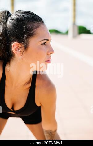Exhausted young female athlete in sportswear bending forward and looking away while having rest during intense fitness workout on street Stock Photo