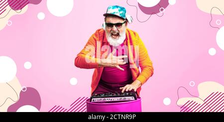 Forever young. Portrait of senior hipster man using devices, gadgets isolated on pink studio background. Tech and joyful elderly lifestyle concept. Bright, modern illustrated background. Stock Photo