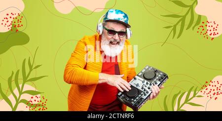 Forever young. Portrait of senior hipster man using devices, gadgets isolated on green studio background. Tech and joyful elderly lifestyle concept. Bright, modern illustrated background. Stock Photo