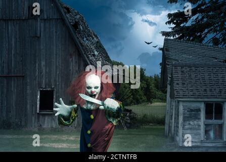 An eerie clown with a knife in the hand in front of a scary scene Stock Photo