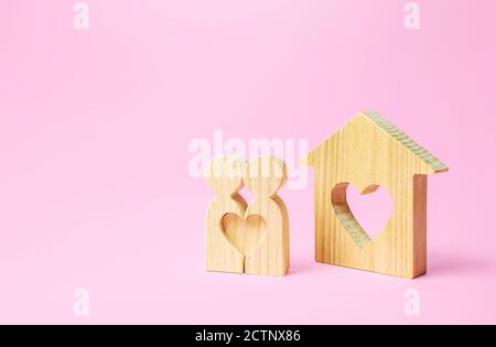 Figures of a love couple stand near house with a heart. Affordable cheap housing for young couples and newlyweds. Stimulating of appearance of new fam Stock Photo