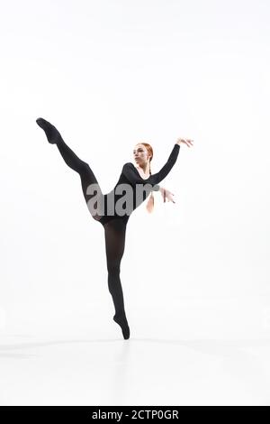 Weightless. Young and graceful ballet dancer in minimal black style isolated on white studio background. Art, motion, action, flexibility, inspiration concept. Flexible caucasian ballet dancer. Stock Photo