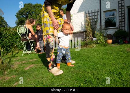 Grandparent and grandchild baby learning to walk family in garden during covid 19 pandemic in autumn sunshine Carmarthenshire Wales UK   KATHY DEWITT Stock Photo
