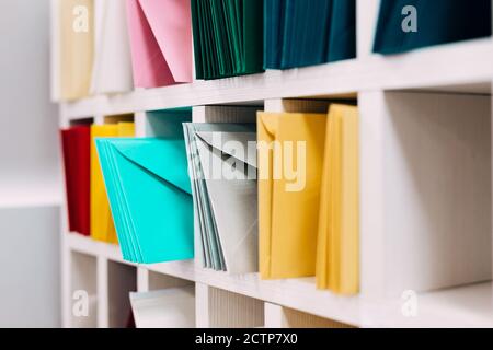 Multiple piles of various postal envelopes arranged on a shelf by color and type categories. Sorted paper mail covers in library/office. Stock Photo