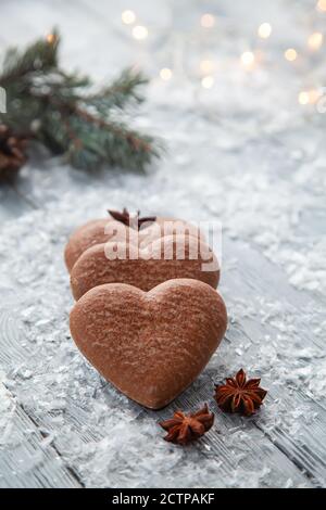 Christmas gingerbread in the form of a heart and a Christmas tree branch on a snowy wooden background Stock Photo