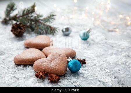 Christmas gingerbread in the form of a heart and a Christmas tree branch with blue balls on a snowy wooden background Stock Photo