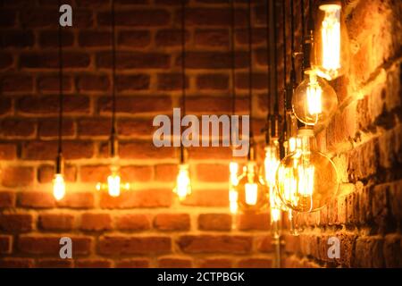 Orange retro lamps hanging on a dark black brick wall background. Vintage incandescent Edison type bulbs. Stock Photo