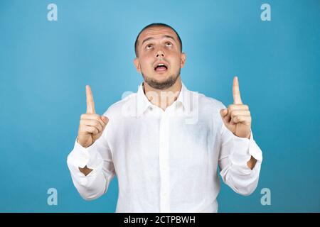 Russian business man wearing white shirt standing over blue background smiling with happy face pointing up with two fingers