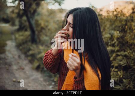Young woman biting a pear in the field wearing a sweater Stock Photo