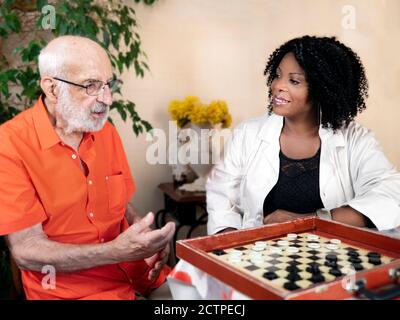 Horizontal portrait of an African American medical assistant playing a board game with an ederly caucasian man Stock Photo