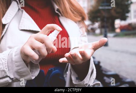 Closeup image of young woman wearing disposable protective face mask and using sanitizer or disinfectant spray walking the street. Pandemic prevention Stock Photo