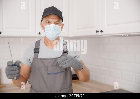 Kitchen installation, worker in medical mask assembling furniture white carved cabinet front Stock Photo