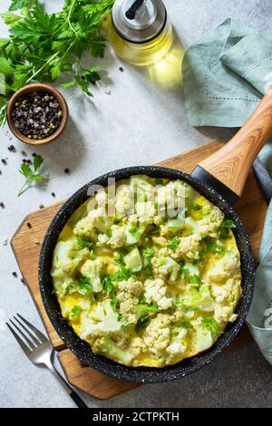 Healthy breakfast or diet lunch. Egg omelet with cauliflower in a cast-iron pan on a light stone table top.