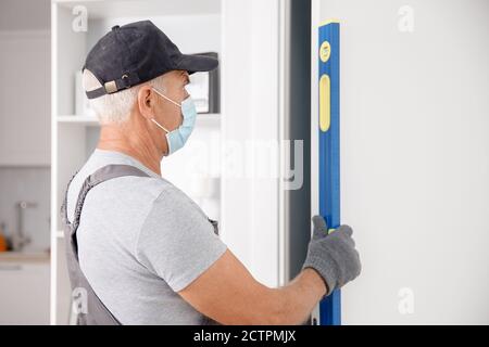 Checking doorway for verticality using bubble level by master carpenter wearing medical mask Stock Photo