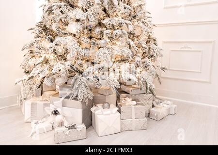 Christmas presents under New Year tree with artificial snow with golden illumination. Silver color Stock Photo