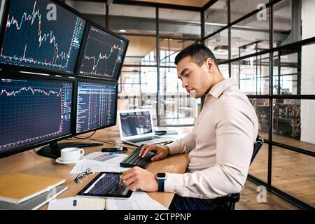 Stock Traiding. Trader sitting at office in front of monitors with data using digital tablet monitoring interpreting and analyzing cryptocurrency Stock Photo