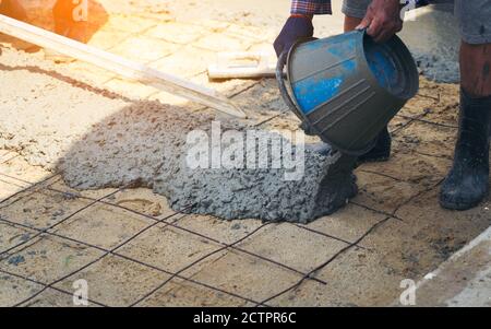 Close up of construction worker's gloved hands using trowel to scrape excess mix level with wood forms freshly poured concrete pad Stock Photo