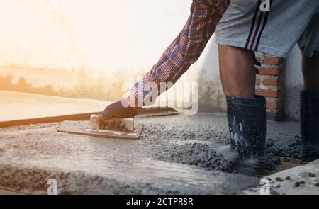 Close up of construction worker's gloved hands using trowel to scrape excess mix level with wood forms freshly poured concrete pad Stock Photo