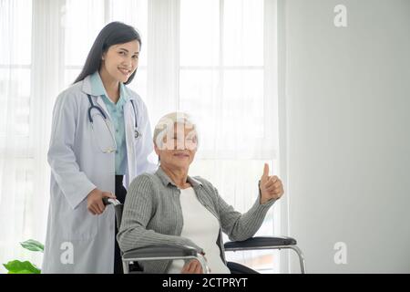 Physiotherapist Looking At Senior Patient Sitting In Wheelchair, doctor and patient on wheelchair Stock Photo
