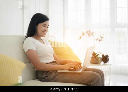 Young lady with modern laptop sitting on sofa at home Stock Photo