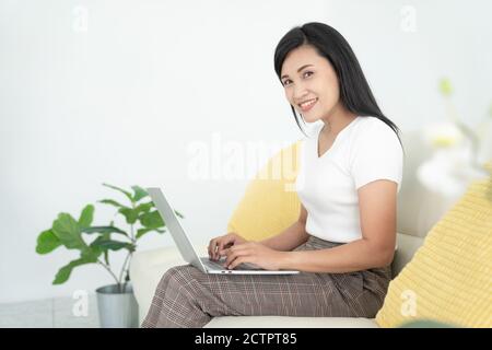 Young lady with modern laptop sitting on sofa at home Stock Photo