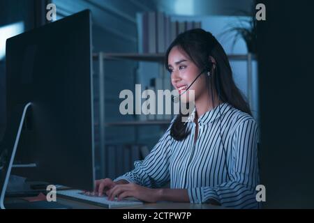 Young Thai Asian customer services care operators working night shift in call center for helping assistance client in workplace at night time Stock Photo